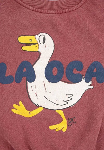 Felpa color bordeaux con un cartone animato di un'anatra bianca con becco e zampe gialle. La scritta "LA OCA" è mostrata in modo prominente in blu scuro.