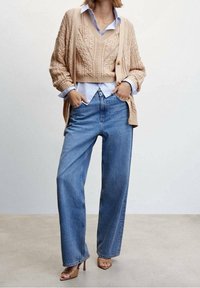 Cardigan beige en tricot, chemise bleu clair à col, gilet beige en tricot. Jean bleu à jambes larges, sandales à talons hauts marron. Style minimaliste.