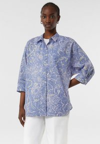 Blue floral print short-sleeve shirt featuring a relaxed fit, button-down front, and white accents on a textured fabric.