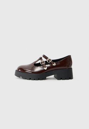Chaussure en cuir verni bordeaux brillant avec un bout rond, des découpes latérales et des accents de boucle en métal. Elle présente une semelle épaisse noire à motifs.