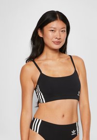 Svart sport-bh med justerbara axelremmar och fyrkantig halsringning, med vita tre-straxiaccents på sidorna och en logodetalj i fållen.