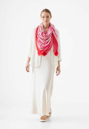 Pink and red patterned scarf with fringed edges, worn over a white shirt and long dress, highlighting its vibrant colors and soft texture.