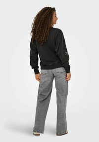 Felpa nera con vestibilità oversize e polsini a coste; jeans grigi a gamba larga con una leggera texture e tasche. Vista posteriore dell'outfit.