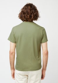Kortærmet olivengrøn t-shirt lavet af blødt stof, med rund halsudskæring og en subtil brandingdetalje på ryggen.