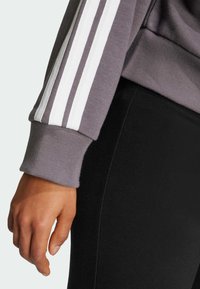 Szara bluza z białymi, trzema paskami na rękawach, połączona z czarnymi legginsami. Miękki materiał i dopasowany krój.