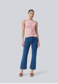 Rosa gemustertes Tanktop mit Raffung, kombiniert mit eng anliegenden blauen Jeans im Bootcut-Stil und braunen Sandalen mit Absatz.