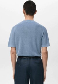 Lehké modré pletené tričko s krátkými rukávy, texturovaným povrchem, kulatým výstřihem a volným střihem, doplněné tmavě modrými kalhotami s knoflíkovými detaily.