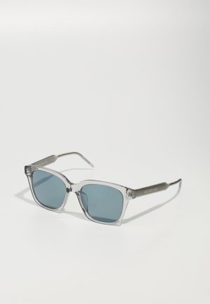 Óculos de sol quadrados com armações transparentes, lentes azuis e braços prateados texturizados com padrões lineares.