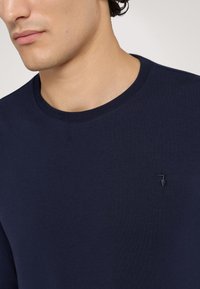 Granatowa bawełniana koszulka z okrągłym dekoltem, z małym haftowanym logo na piersi oraz gładką, miękką teksturą.