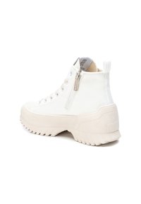 Zapatilla alta blanca de lona con suela de goma texturizada, cierre de cremallera y refuerzo en el talón, que presenta un sutil logotipo de la marca en la lengüeta.