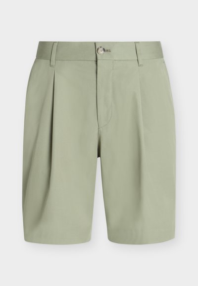 Shorts vert clair, cintrés, avec plis, passants pour ceinture, fermeture par bouton et fermeture éclair cachée à l'avant sur fond uni.