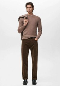 Suéter marrón de canalé combinado con pantalones de pana marrones. Zapatos negros y un suéter gris colgado sobre el hombro. Atuendo sencillo y casual.