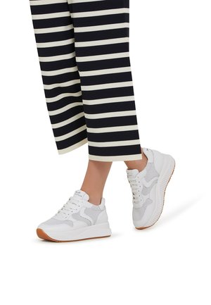 Baskets blanches avec un dessus en maille texturée, un collier rembourré et une semelle en caoutchouc. Associées à un pantalon large rayé bleu marine et crème.