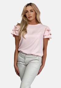 Jasnoróżowa bluzka z krótkim rękawem z warstwowymi falbanami na rękawach, połączona z jasnymi, dopasowanymi spodniami, gładki materiał i luźny krój.