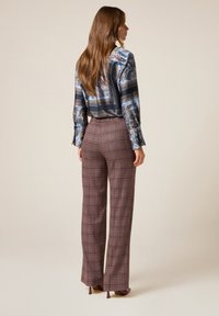 Blusa azul con estampado y mangas largas, combinada con pantalones de cuadros burdeos de pierna ancha y cintura alta, y tacones a juego.