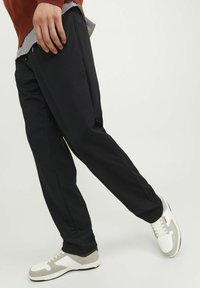 Pantaloni neri realizzati in un materiale morbido, con una cintura elastica e tasche laterali. Abbinati a scarpe da ginnastica bianche e grigie.