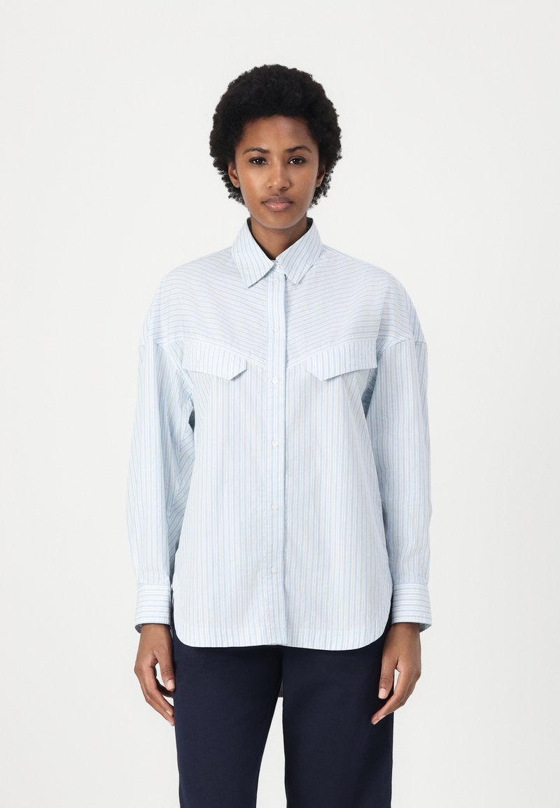Camicia a righe blu chiaro con colletto classico, chiusura con bottoni sul davanti e due tasche sul petto. Maniche lunghe con polsini abbottonati. Tessuto morbido.