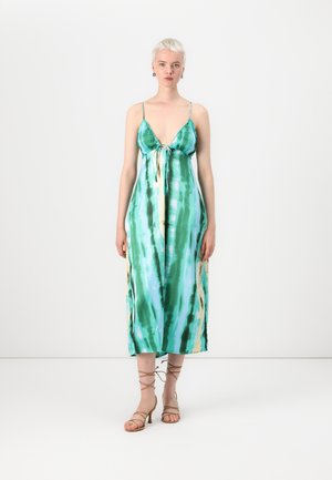 Robe décontractée sans manches en tie-dye vert et bleu avec un décolleté plongeant, des bretelles ajustables et des fentes sur les côtés. Associée à des sandales à lanières beiges.