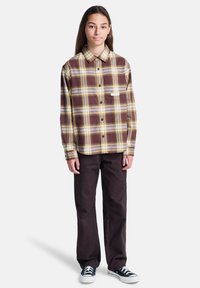 Rutigt flanellskjorta i nyanser av brunt och gult, knäppes-up design, bar med mörkbruna byxor och svarta sneakers.