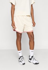 Αθλητικό σορτς χρώματος κρέμας με ροζ περιθώριο, σετ με φαρδιά κρέμα μπλούζα, μαύρα/λευκά αθλητικά παπούτσια και λευκές κάλτσες.