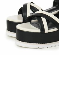 Sandali platform bianchi e neri con design a fasce incrociate, realizzati in pelle liscia. Presentano una suola spessa e una suola esterna bianca texturizzata.
