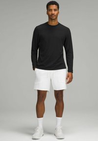 Cămașă neagră cu mânecă lungă, asortată cu pantaloni scurți albi. Cămașa are o textură netedă; pantalonii scurți au șnur și buzunare laterale. Adidașii albi completează ținuta.
