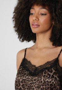 Camisole s leopardím vzorem z lesklé látky, s černým krajkovým lemováním kolem výstřihu. Nastavitelné tenké ramínka pro dokonalé usazení a pohodlí.