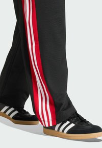 Svarta träningsbyxor med röda sidostripe, utrustade med tre vita ränder. Matchade med svartvita sneakers som framhäver ett texturerat material.