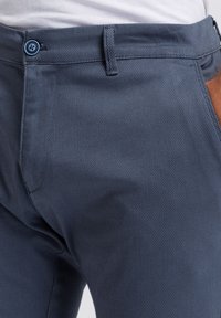 Marineblaue strukturierte Hose mit einem dezenten Netzmuster, mit flacher Vorderseite, Reißverschluss und einem blauen Knopf am Bund.