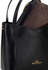 Schwarze Ledertasche mit strukturiertem Finish, ausgestattet mit einem Logo in goldfarbenem Ton und einem braunen Innenbeutel mit Reißverschluss.