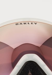 Oakley-briller med rosa gradient-linse, hvit ramme og strukturert svart skuminnvendig. Har en fremtredende logo på toppen.
