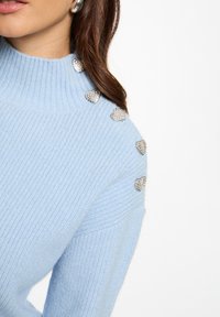 Maglione azzurro chiaro con colletto alto, texture a coste e decorazioni a forma di cuore in strass argentati lungo la cucitura della spalla.