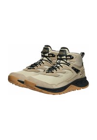 Helle beige Wanderschuhe mit schwarzen Akzenten, einer strukturierten Oberseite, einem gepolsterten Schaft und einer stabilen Gummisohle mit einem dreieckigen Profil.