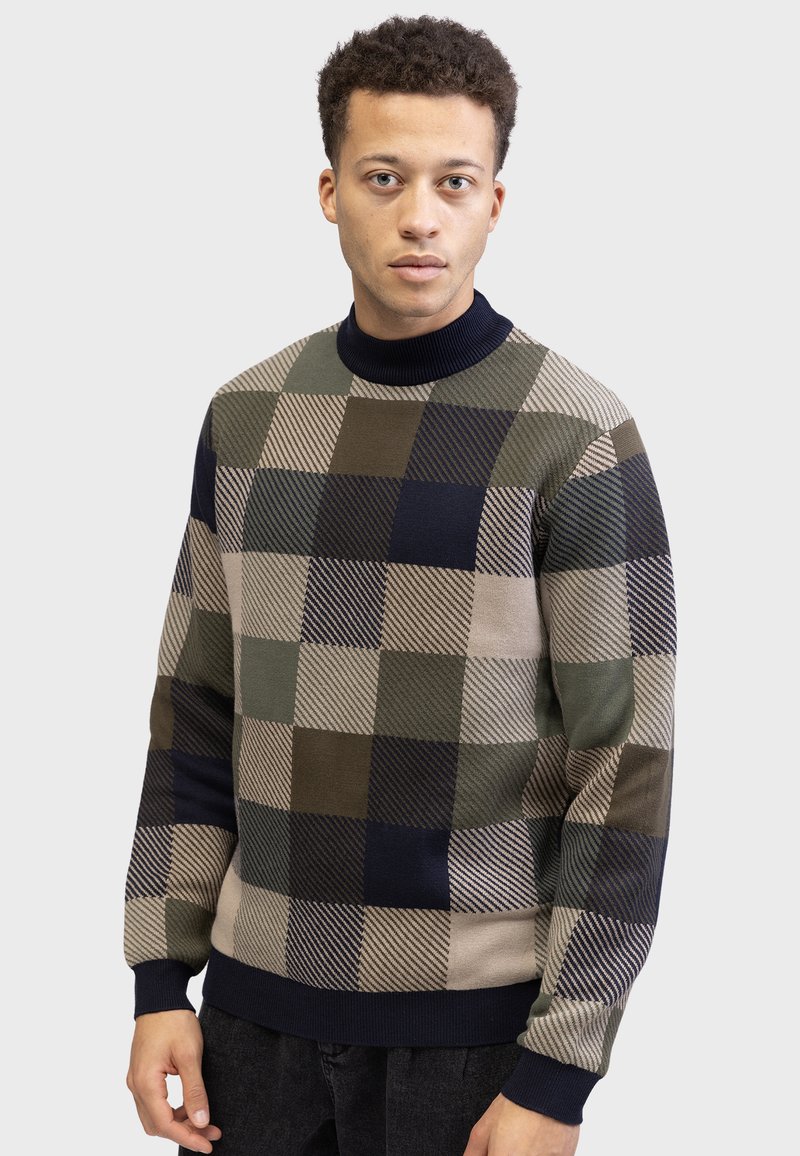 Pull en tricot avec un col montant, présentant un design en patchwork de motifs géométriques verts, bleus et beiges. Poignets et ourlet côtelés.