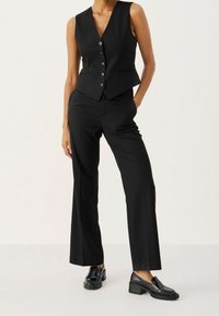 Svart skräddarsydd väst med v-ringning, femknappsstängning och sidofickor, kombinerad med raka svarta byxor och svarta loafers.
