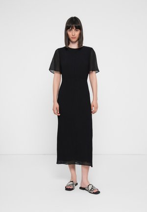 Black midi dress with short, sheer sleeves, textured fabric, fitted waist, and a straight hem. Paired with black and white patterned sandals.
