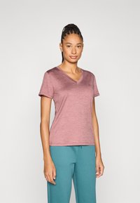 Μπλουζάκι V με κοντά μανίκια σε αποχρώσεις μουβ, κατασκευασμένο από ελαφρύ ύφασμα, συνδυασμένο με μπλε-πράσινη φόρμα. Απλός σχεδιασμός με διακριτική εμπορική σήμανση.