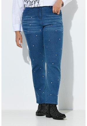 Vaqueros azules de mezclilla con adornos de perlas dispersas, combinados con botas negras de tobillo decoradas con puntos blancos.