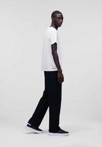 T-shirt alb din bumbac cu mâneci scurte, combinat cu pantaloni negri, cu croi lejer, și teniși negri, stând pe un fundal simplu.