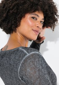 Maglia grigia a maniche lunghe in tessuto morbido e testurizzato con una leggera trasparenza. Girocollo e dettagli di vestibilità rilassata sulle spalle.