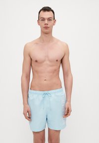 Lys blå badetights med elastisk midje og snøring, med hvit logo trykk på venstre side. Glatt stofftekstur.