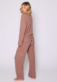 Set di loungewear a coste in rosa polveroso, composto da una maglietta a maniche lunghe con vestibilità rilassata e pantaloni a gamba larga, entrambi realizzati in morbido tessuto lavorato a maglia.