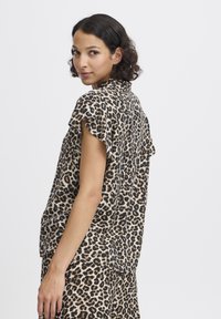 Blouse à imprimé léopard avec des manches courtes à volants, un col et une coupe décontractée. Fabriquée en tissu léger avec une texture douce.
