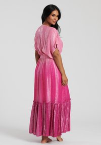 Rosa maxiklänning med korta dolmansärmar, texturerat tyg och volangslut, prydd med paljetter för en glittrande effekt.