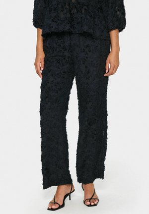 Schwarzes, strukturiertes Zweiteiler-Outfit mit Blumenmustern. Die Bluse hat puffige Ärmel, während die Hose locker geschnitten und knöchellang ist.