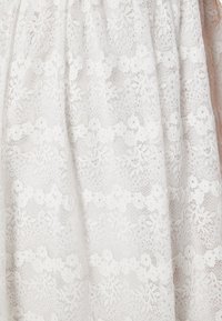 Biała koronkowa tkanina z kwiatowymi wzorami i misternymi detalami, prezentująca półprzezroczystą teksturę o delikatnym, warstwowym wyglądzie.