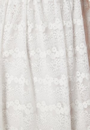 Tessuto in pizzo bianco con motivi floreali e dettagli intricati, che presenta una texture semitrasparente con un aspetto delicato e a strati.