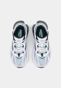 Sneaker bianche in mesh con accenti neri e suola texturizzata. I lacci sono bianchi con un anello centrale. Marchio visibile sulla linguetta e sulla soletta.
