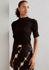 Black ribbed top with short puff sleeves, paired with a black skirt featuring a white diamond pattern. Soft texture, fitted design.