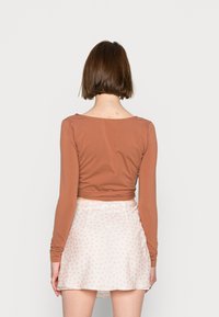 Top cropped de mangas longas castanho, combinado com uma saia branca com um pequeno padrão floral rosa. Tecido leve e suave com um design ajustado.